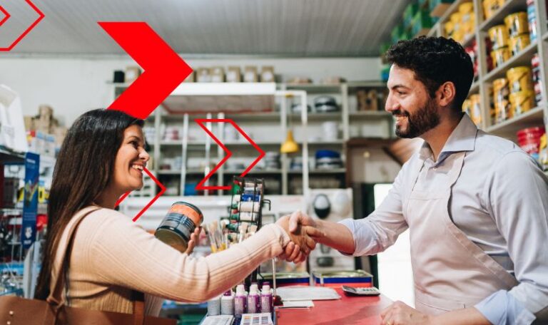 Vendedor cumprimenta cliente satisfeita em loja de materiais, simbolizando a fidelização de clientes por meio de um bom atendimento, relacionamento próximo e experiências de compra positivas.