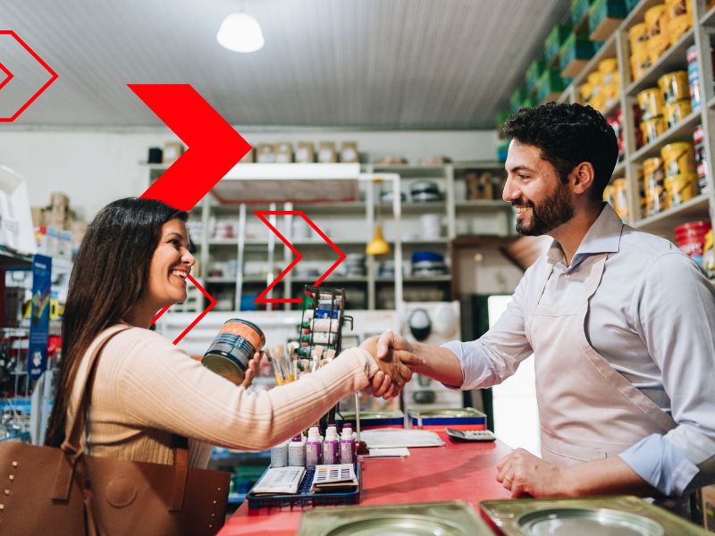 Vendedor cumprimenta cliente satisfeita em loja de materiais, simbolizando a fidelização de clientes por meio de um bom atendimento, relacionamento próximo e experiências de compra positivas.