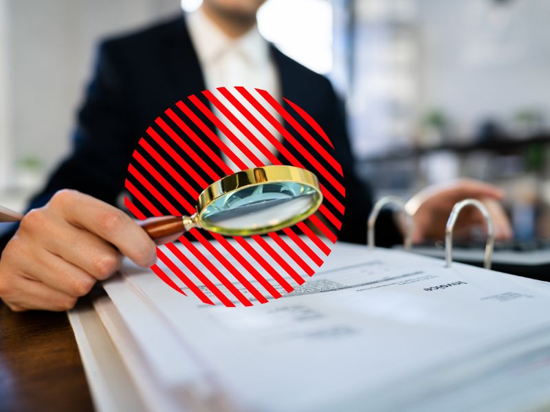 Profissional analisa documentos fiscais com lupa sobre mesa de trabalho, representando a substituição tributária como mecanismo de fiscalização e controle na apuração e recolhimento antecipado de impostos.