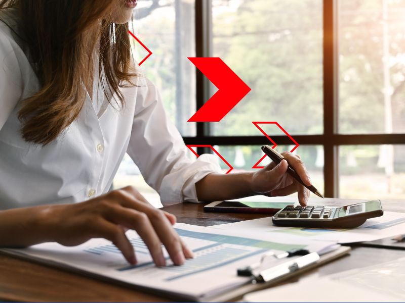 Profissional analisa documentos financeiros e utiliza calculadora durante o fechamento de caixa, conferindo entradas, saídas e saldos para garantir a precisão do controle financeiro empresarial. O processo contribui para a conciliação financeira, reduz divergências e apoia uma gestão financeira mais eficiente.