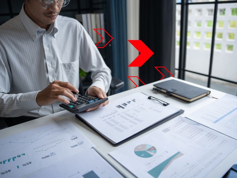 Profissional analisa relatórios financeiros e realiza cálculos em ambiente corporativo, representando o controle de custos para acompanhar despesas, identificar oportunidades de economia e melhorar a rentabilidade da empresa.