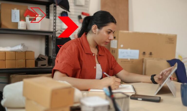 Profissional registra informações manualmente enquanto consulta dados em dispositivo eletrônico, representando processos manuais que aumentam o risco de erros, retrabalho e perda de produtividade na gestão empresarial.
